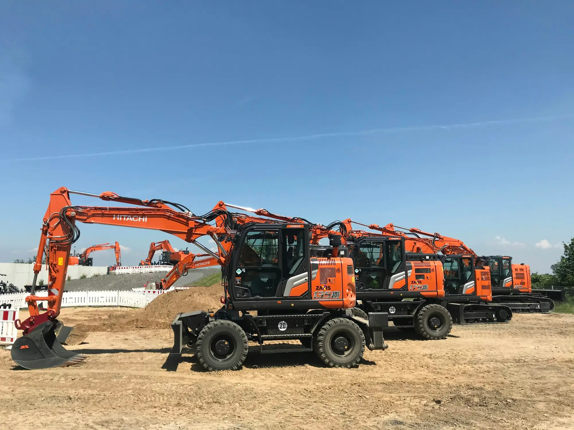 Row of orange excavators parked on a dirt work site under a clear blue sky